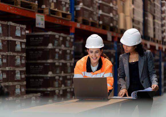 Diverse warehouse team analyzing stock data on a digital tablet. African manager and Middle Eastern employee collaborate on inventory management, logistics planning, and operational efficiency in a modern distribution center.