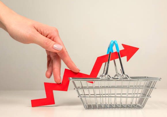 The fingers of a woman's hand step up the arrow of a chart lying on a shopping basket. Crisis and rising commodity prices concept